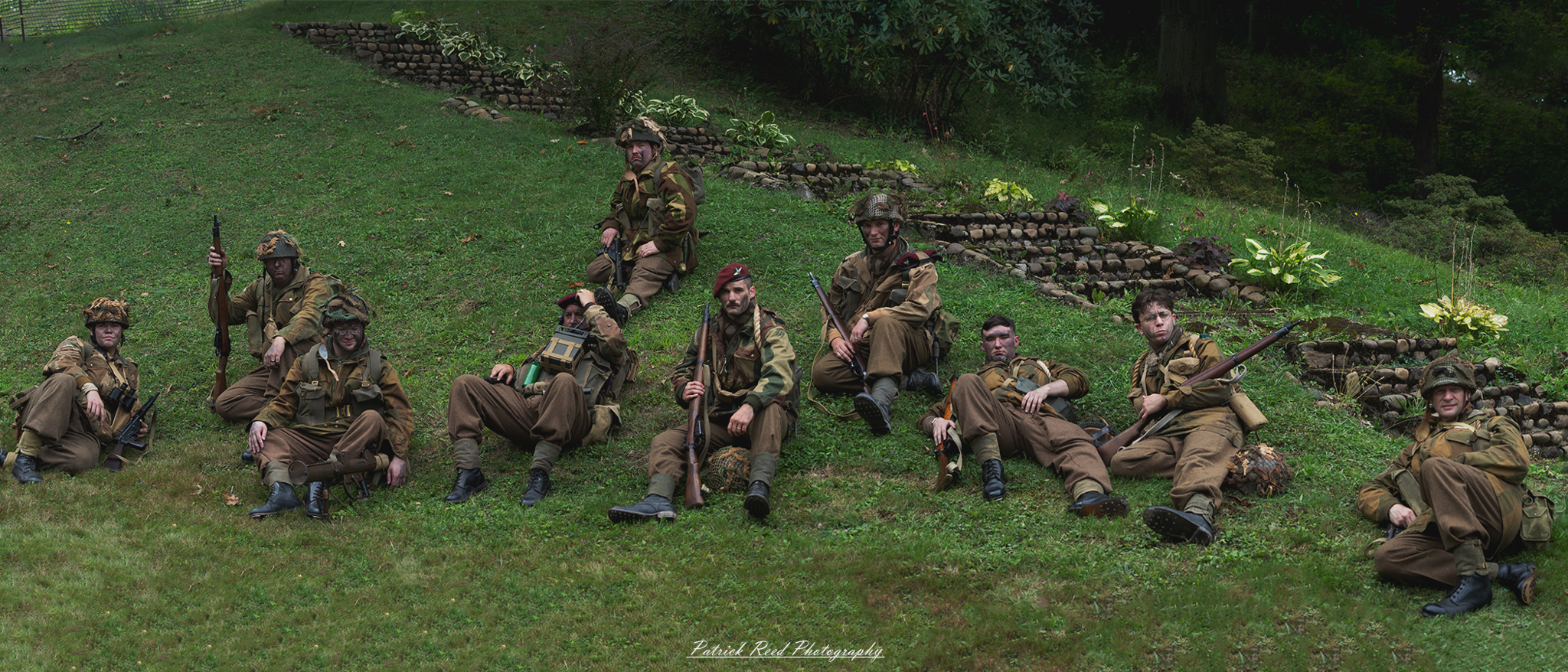 Soldiers relaxing on the grass, some lying back and others sitting up, enjoying a moment of respite. The scene captures a sense of camaraderie and relief amidst the pressures of military life, showcasing their human side during downtime.